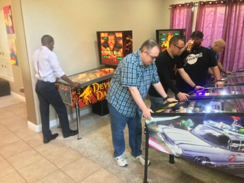Four players crowded around a machine in a host's game room