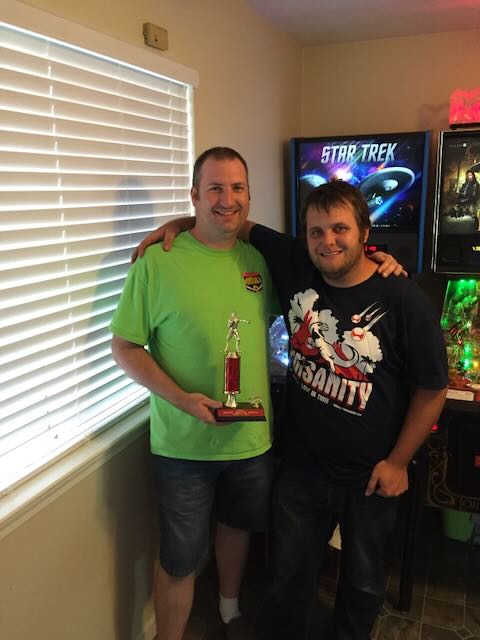 Two players posing with a trophy, a Star Trek machine behind them