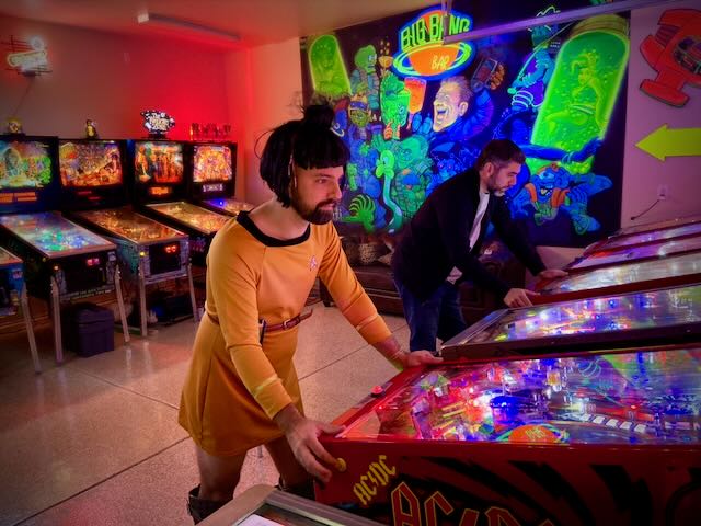 A player in an orange jumpsuit at the flippers under coloured lights